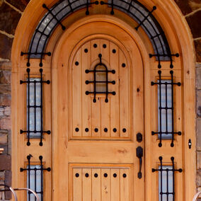 Custom arched wooden door by Dallas Millwork with decorative iron accents, set within a stone entryway