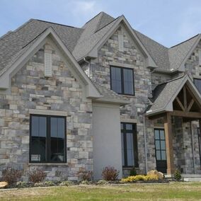 Modern home with gray, tan, and white stone veneer exterior, black windows, and cedar beams on entry porch.