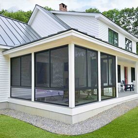 A modern white home with a metal roof and a spacious wraparound porch, featuring the Summer Space Porch Enclosure System with large black-framed screens, creating a comfortable, outdoor living space