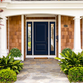 Front entrance with a navy blue Reeb exterior door framed by white columns and surrounded by lush greenery