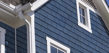 Close-up of home exterior with blue vinyl siding and white trim around windows