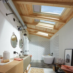 Pictured is a modern bathroom with Velux skylights and a wooden ceiling, with natural light