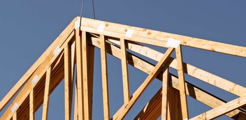 Pictured is a pair of wood trusses hoisted against a clear blue sky before being placed.